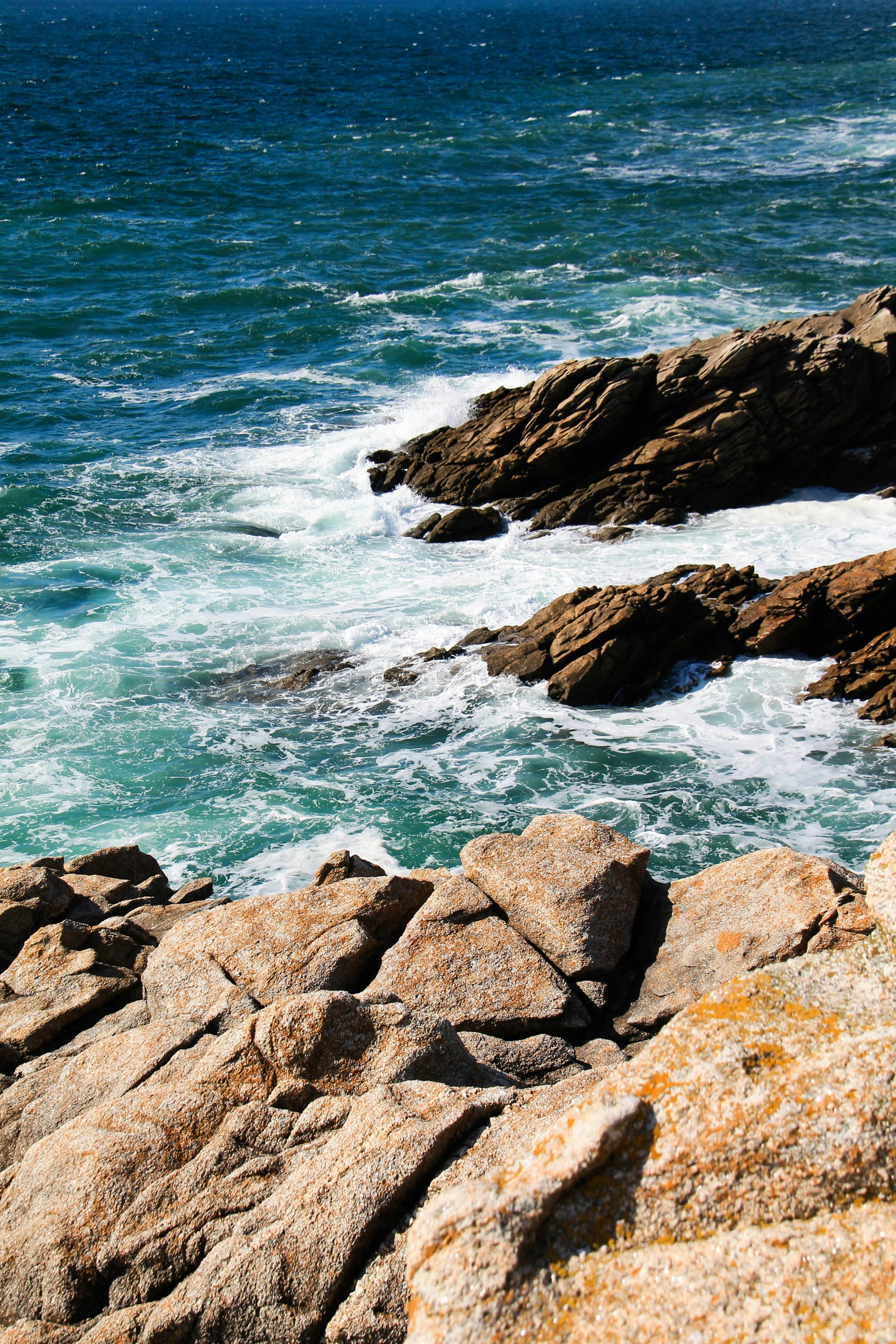 brown rocky shore with ocean waves crashing on rocks during daytime
